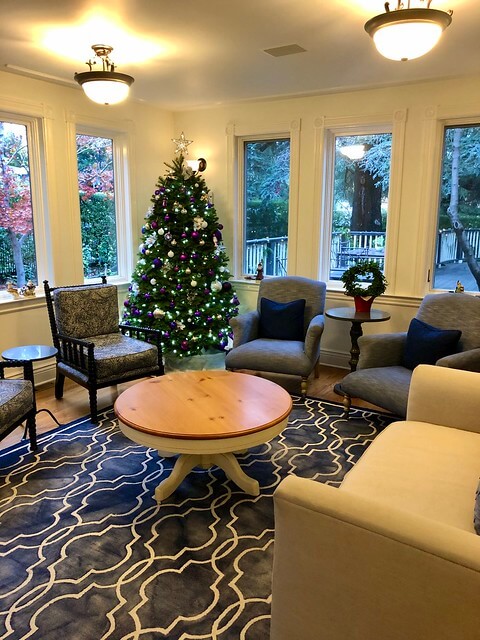 Christmas tree with ornaments and lights sits in the corner of the Queen Ann Victorian parlor.