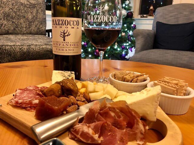 Charcuterie platter with Mazzocco Zinfandel bottle and red wine glass with Christmas tree in background.