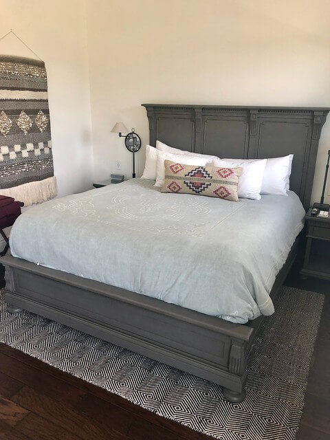 Antiqued grey oak bed frame on king bed, decorative tapestry on wall. 