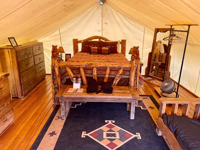 Hand-carved wood bed frame with queen size mattress rests inside a heated canvas glamping tent with Western-themed wool rug at The Bar W Guest Ranch in Whitefish, Montana. 