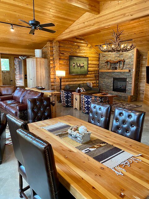 Rustic luxury at Elk Lakeside Cabin with dark leather chairs, wood dining table, rock fireplace in living room with elk shed chandelier. 