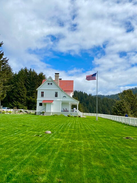 Two-story Heceta Lighthouse Bed and Breakfast with American flag and green lawn in Yachats, Oregon.