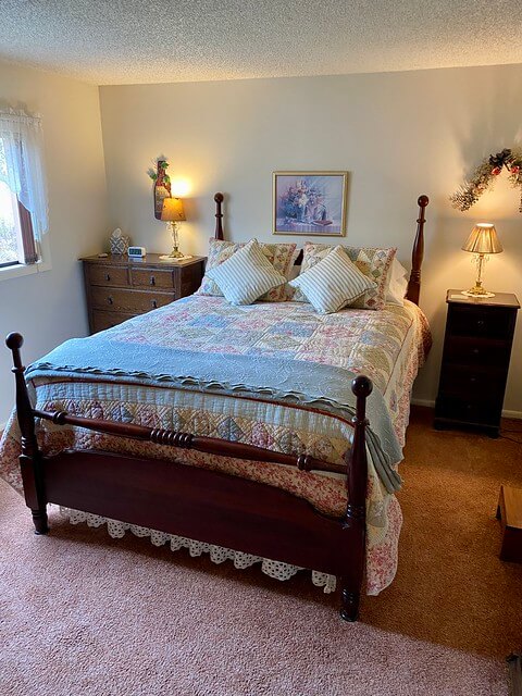 Queen bed with hand-stitched quilt and 2 blue and white stripped accent pillows.