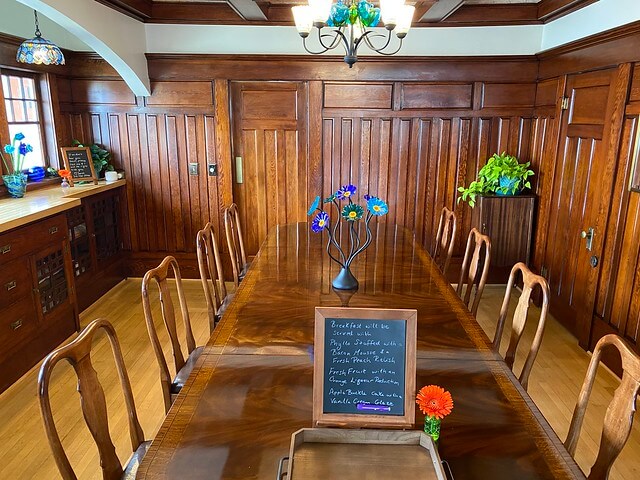 Wood-paneled dining room and stained glass art frame the wood dining table at Edwin K Bed & Breakfast. nd 8 wood chairs 