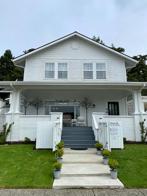 Open porch with tapered columns is a signature feature of Edwin K Bed & Breakfast, a 1914 Craftsman style, 2-story white house in Florence, Oregon.