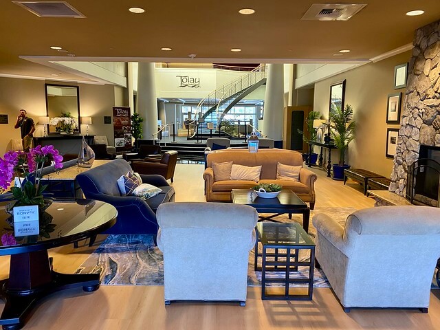 Sheraton hotel lobby with blue and beige sofas and two chairs for lounging next to the rock fireplace. Tolay restaurant entrance and staircase in the background.