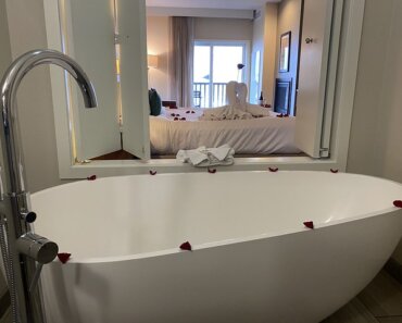 Rose-petal decorated white bath tub with wood-shuttered window opening to the king deluxe suite at Inn at Nye Beach.