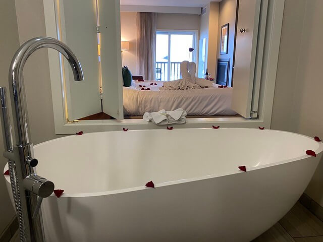 Rose-petal decorated white bath tub with wood-shuttered window opening to the king deluxe suite at Inn at Nye Beach. 