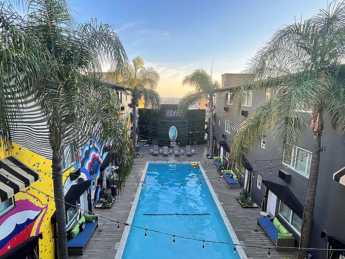 A rectangular pool is surrounded by the three-story Hotel Ziggy. A large mural covers one of the walls.