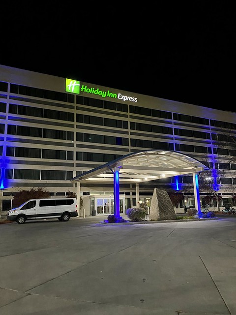 The exterior of the 6-story Holiday Inn Express Boise University hotel at night. A white van is parked in front of the hotel, to the left of the hotel portico. 