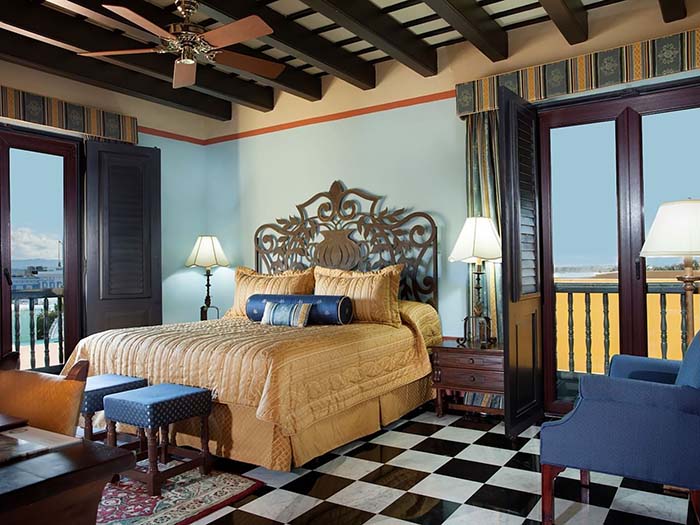 Large bed in blue bedroom with ornate wood headboard and black and white checkered floor