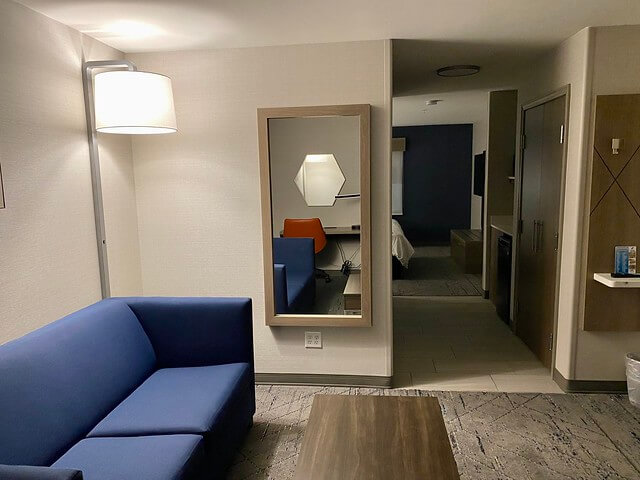 Grand Junction hotel king suite living area with blue sofa, oblong wood table, floor lamp and full length mirror on wall.