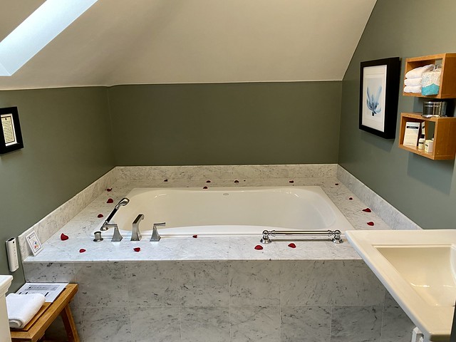 Red rose petals are scattered around the edge of the Jacuzzi bathtub within the Majestic Suite at Majestic Inn & Spa. 