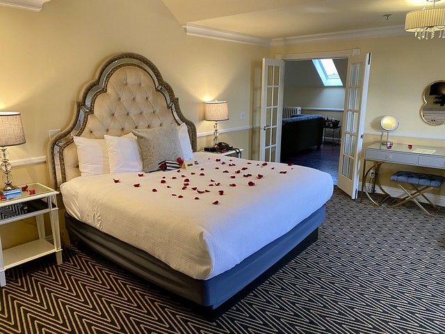 King bed with white bedspread, covered in red rose petals.