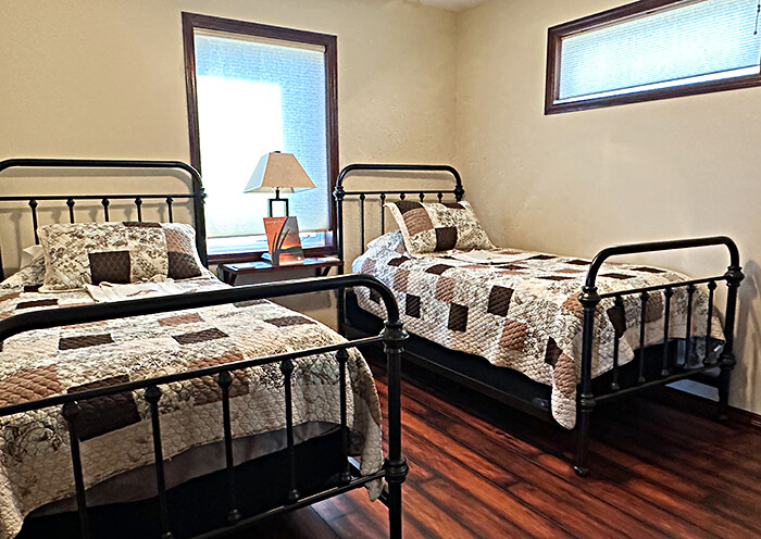 A small bedroom with two single beds, vintage-style metal bed frames, and country-style quilts