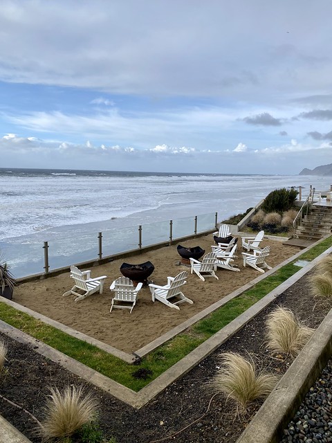 Three outdoor fire pits with three, white Adirondack chairs around each fire pit. Cement stairs are below the handicap-accessible firepit above the 3 firepit stations. 