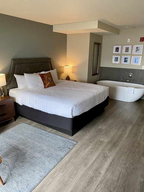 King bed in oceanfront suite. A white soaking tub sits behind the king bed with white bedspread and four white pillows. 