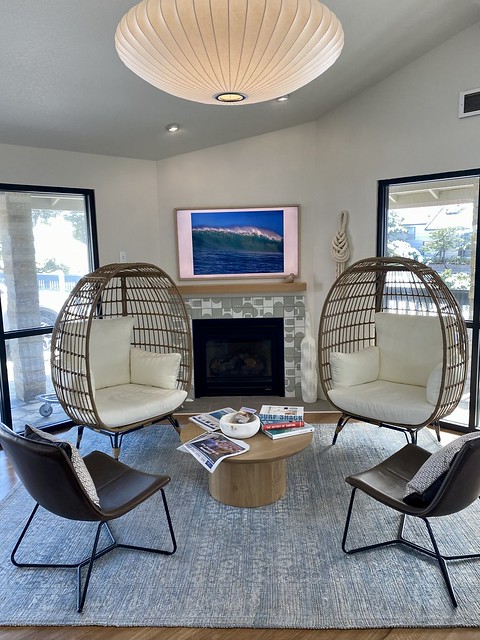 Hotel lobby with 2 wicker, egg-shaped chairs next to gas fireplace. Two modern chairs with bucket seating are placed across from the wicker chairs. An area rug ties the room together. 