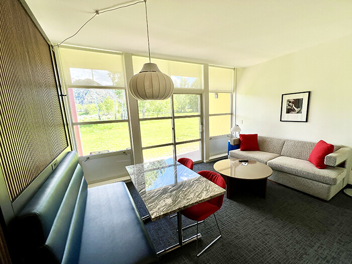 Living area in a hotel room with blue leather seating and table and red pillows on a couch. 