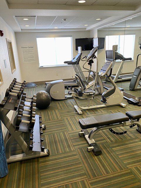 Three Precor exercise machines in the hotel fitness room, along with a workout bench and hand weights. 