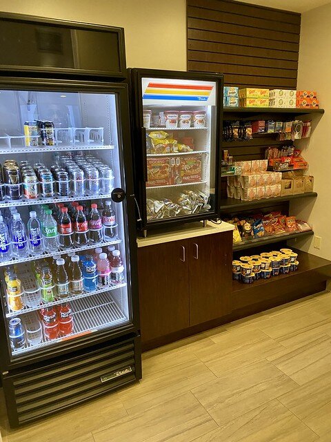 Hotel snack bar with refrigerated drink case, freezer case with pizza and dry goods shelf with candy, mac & cheese containers and chips. 