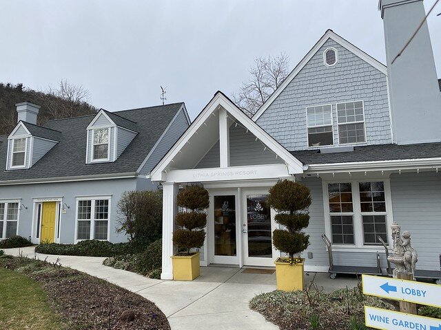 Entrance to Lithia Springs Resort. Single story hotel entrance with 2 white pillars, 2 double glass doors and 2 topiary plants with yellow pots in from of the resort entrance. 