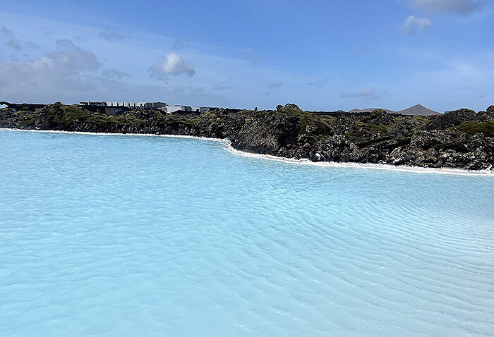 Bright milky blue lagoon abutting lava rock with blue sky overhead