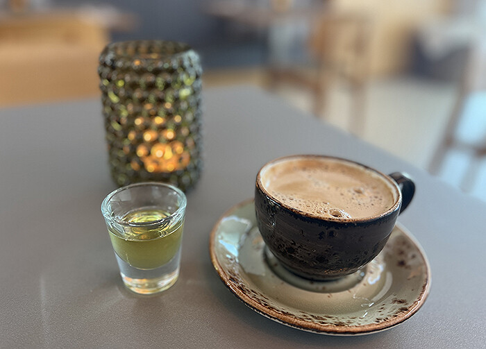 Frothy coffee in pottery-style cup and saucer with shot glass of cod liver oil