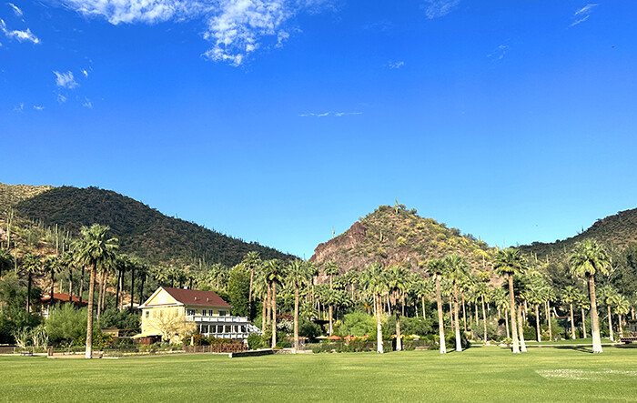 Yellow lodge surrounded by palm trees, green lawns, and mountains