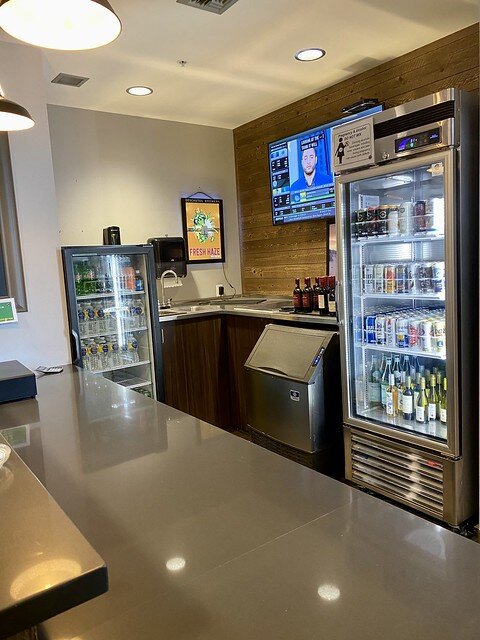 Go Marketplace 2 refrigerated, glass front coolers of bottled water, beer and wine. a stainless steel countertop. A small, flatscreen tv is above the ice machine. 