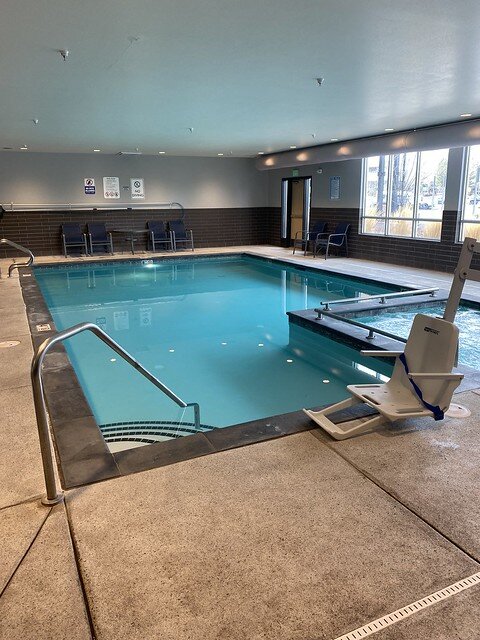 Peppertree Inn indoor swimming pool. The handicapped accessible chair lift is next to the entrance to the whirlpool. Metal handrail attaches to four steps into the pool. 