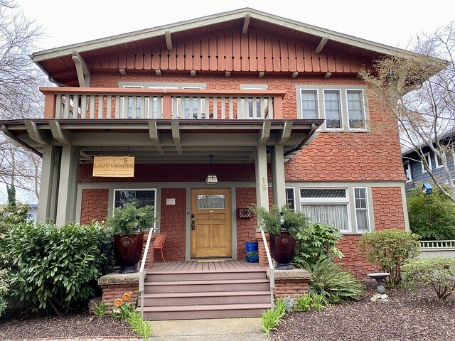 Front of historic Lady Geneva Bed and Breakfast. The 2-story craftsman style home has wood siding painted a tomato color. 