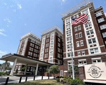 Large brick historic building with white windows and American flag in front.