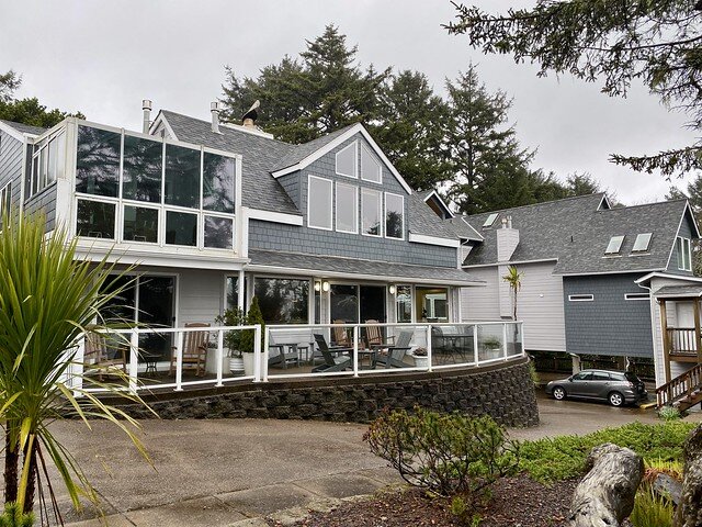 Walls of glass and wood shingles cover the back of Ocean House in Newport. A cement retaining wall and cement driveway lead to the underground parking of the inn. A grey SUV is parked in the underground parking area. 