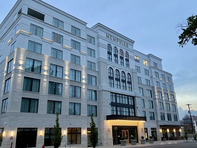 Seven stories of square, glass windows are on the exterior of the hotel. White building with glass windows photographed at dusk from street level. 