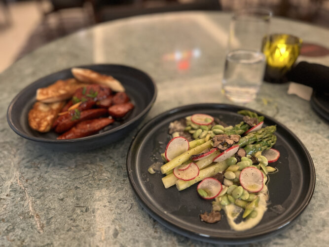 Two plates of food: asparagus and edamame and chorizo with baguette