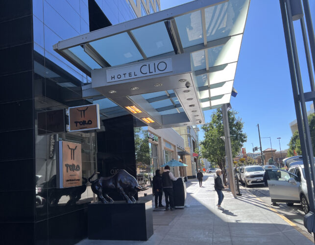 Sidewalk and entrance to a city hotel with bright blue sky in background.