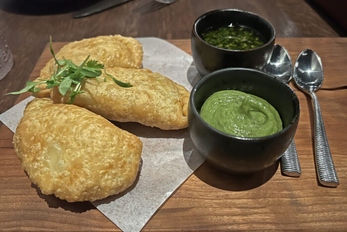 Flaky empanadas on a wooden board with two small ramekins of green sauce