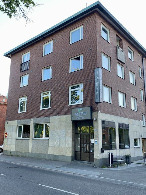 Three-story rectangular cement and brick building. The front door is on the right of the building entrance. Nine rectangular windows are set in the front of the brick hotel. 