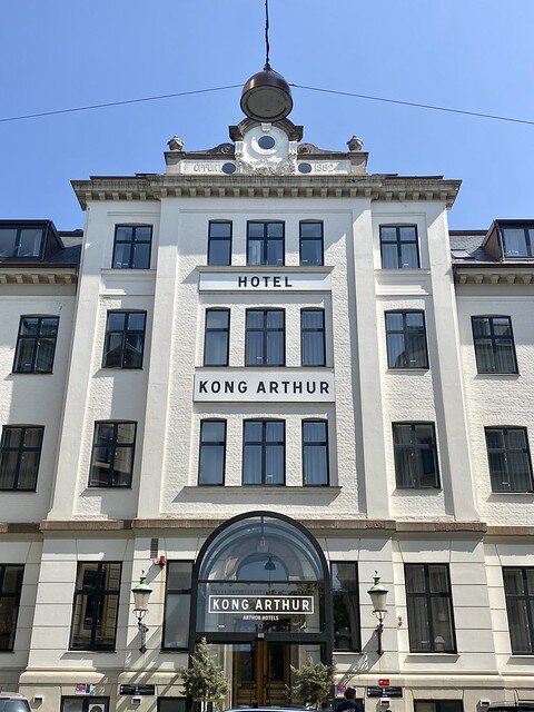 Exterior of Hotel Kong Arthur front entrance. Four story white hotel with name of hotel spelled out in black letters on exterior wall.