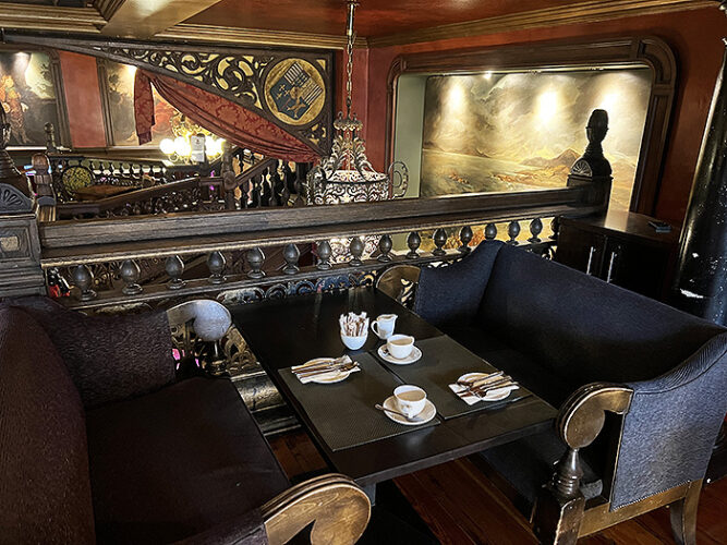 Dark wood table with restaurant setting and ornate woodwork and wall decor. 