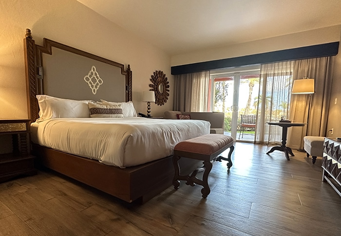 A hotel room with plush bed, wood floors and glass doors that lead to patio and garden