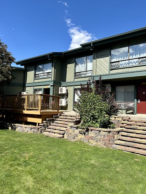 Photo of BW Tree House from the grass-covered courtyard looking into the 2-story green-painted hotel. Concrete pavers with 8 steps, lead to the wood deck outside of my hotel room. Two small air-conditioning units are mounted to the exterior hotel wall. 