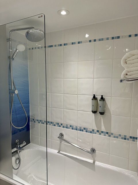 Holiday Inn hotel bathtub and shower combination. Waterfall rain shower overhead and handheld shower wand. A grab bar and shampoo and conditioner bottles were mounted on the white ceramic tiled shower wall. 