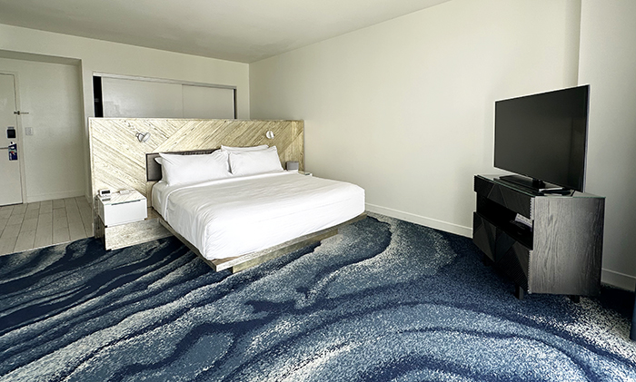 King bed with white linens and blue wall-to-wall carpeting