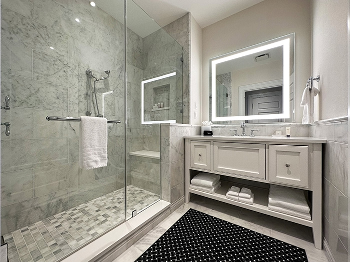 A large white bathroom clad in marble with a glass enclosed shower