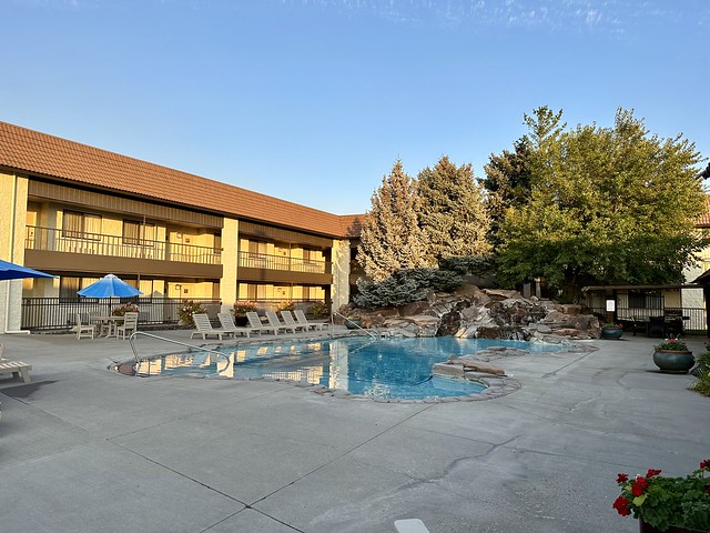 Best Western Foothills Inn outdoor swimming pool with several pine trees. Two-story hotel rooms are behind pool. 