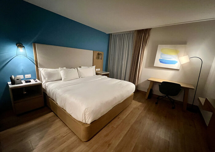 Contemporary hotel room with bright blue accent wall, white bedding, light wood floor