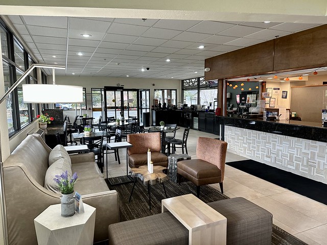 Best Western Alpenglo hotel lobby. Five square and rectangular tables, with 4 black chairs are by the front door entrance. Items from a breakfast buffet wait for morning guests to arrive next to the reception desk of the hotel. A grey leather sofa sits across from 2 chairs and a small faux wood, circular coffee table are across from the reception desk. 