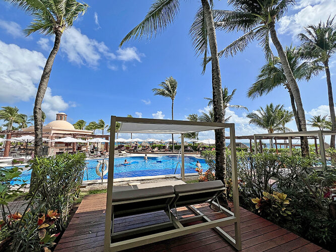 Hotel room deck with cabana bed in front of a turquoise pool with blue sky at Excellence Riviera Cancun.